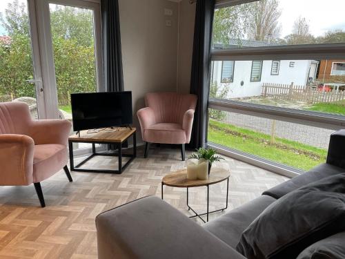 een woonkamer met een bank, 2 stoelen en een tv bij Charming chalet with spacious garden on a holiday park near the Wadden Sea in Hippolytushoef