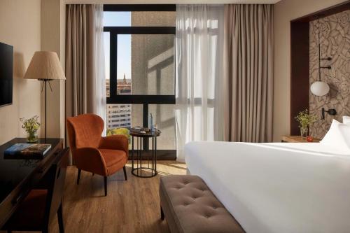 een hotelkamer met een bed, een stoel en een raam bij NH Collection Sevilla in Sevilla