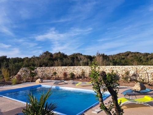 a swimming pool in front of a stone wall at Chalet n * 1 au cœur du maquis in Bonifacio