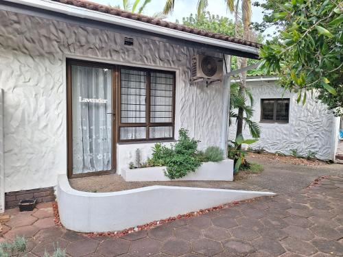 Umuzi Guest House في خليج ريتشاردز: منزل أبيض صغير مع نافذة ونباتات