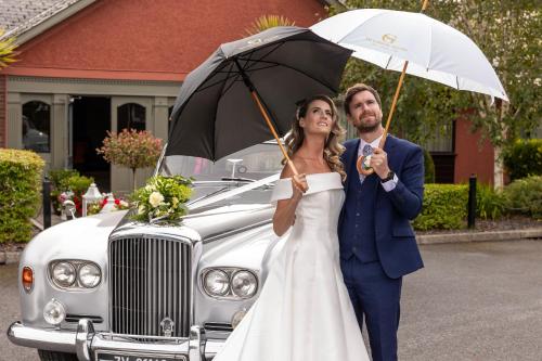 a bride and groom holding umbrellas next to a car at The Glenside in Drogheda