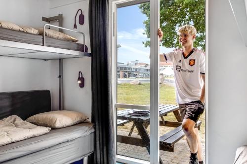 a young man standing in a tiny bedroom with a window at Sportsby Vejen - Danhostel, huse og lejligheder in Vejen