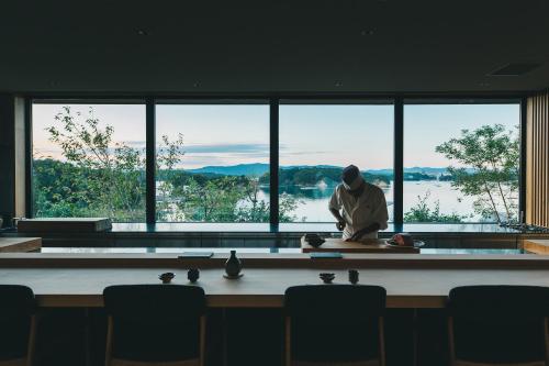 un hombre sentado en una mesa frente a una gran ventana en MOKU ISESHIMA ーl モク伊勢志摩 lー, en Shima