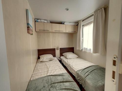 deux lits dans une petite pièce avec une fenêtre dans l'établissement Mobilhome Cocooning, à Mimizan
