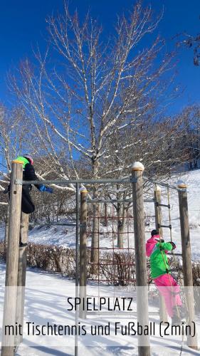 two people jumping over a fence in the snow at Almchalet mit Pool und Sauna in Missen-Wilhams