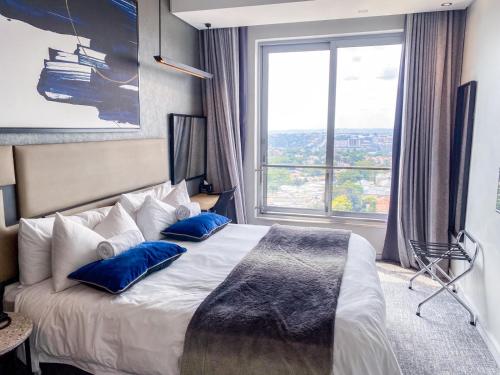 a bedroom with a bed with blue pillows and a window at Cosy Executive Hotel Room (SA) in Johannesburg