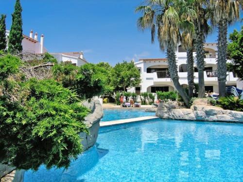 a swimming pool with palm trees and a building at Apartamento en Cala en Porter Menorca in Cala en Porter