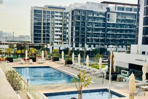 a hotel pool with chairs and buildings in the background at Comfy 1BR in Azizi Riviera 8, Al Merkadh by Deluxe Holiday Homes in Dubai