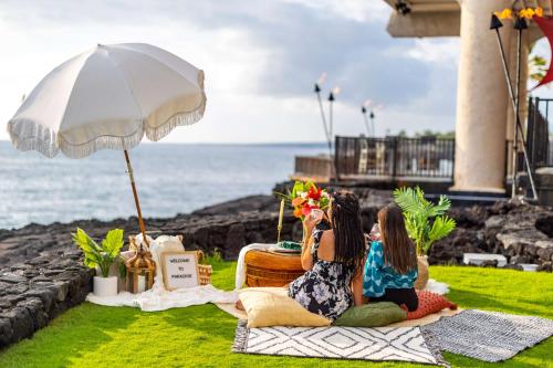 two women sitting on the grass taking a picture of the ocean at OUTRIGGER Kona Resort and Spa in Kailua-Kona