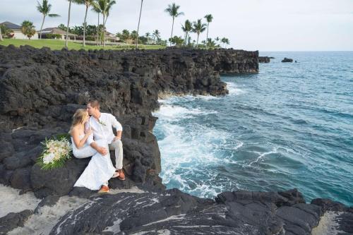a bride and groom sitting on a rock by the ocean at OUTRIGGER Kona Resort and Spa in Kailua-Kona
