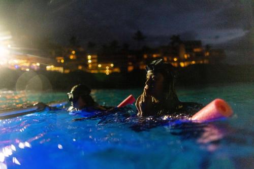two people laying in the water in a swimming pool at night at OUTRIGGER Kona Resort and Spa in Kailua-Kona
