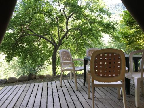 a table and chairs on a deck with a tree at Camping Les Fines Roches in Roquestéron