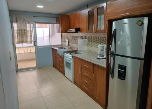 La cuisine est équipée d'un réfrigérateur en acier inoxydable et de placards en bois. dans l'établissement Departamento Gigante de 4 dormitorios. Ecualodge 23, à Cuenca