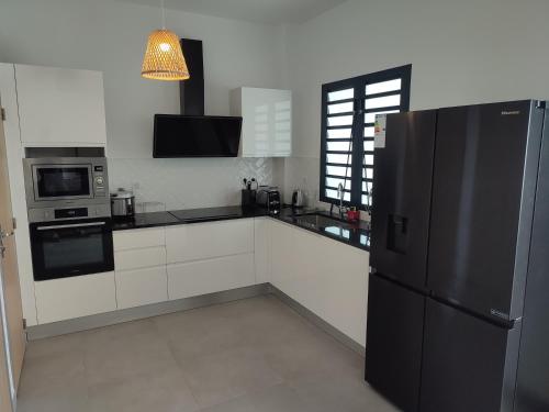 uma cozinha com armários brancos e um frigorífico preto em Lodge Tamarins em Saint-Pierre