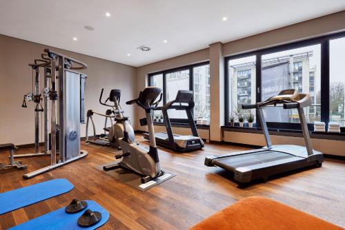 a gym with treadmills and exercise equipment and windows at LÉGÈRE HOTEL Bielefeld in Bielefeld