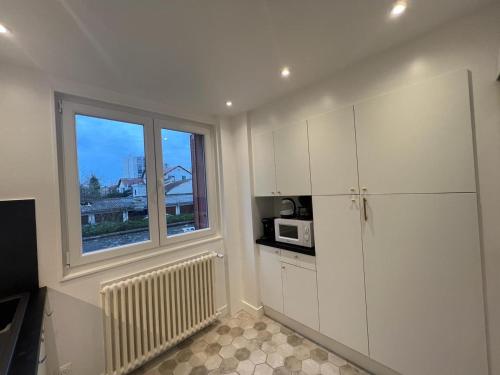 une cuisine avec des armoires blanches et une fenêtre dans l'établissement Appartement Chaleureux Portes de Paris, à Aubervilliers