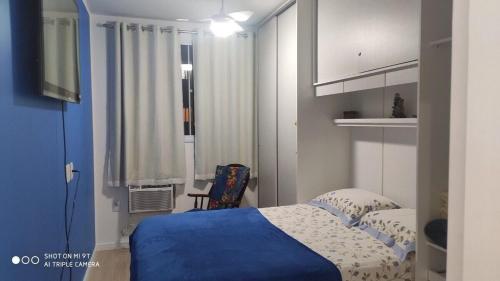 Un dormitorio con una cama azul y una ventana en Apt 2 qtos, prox. ao Rio centro, Jun, e P. Olimpic en Río de Janeiro