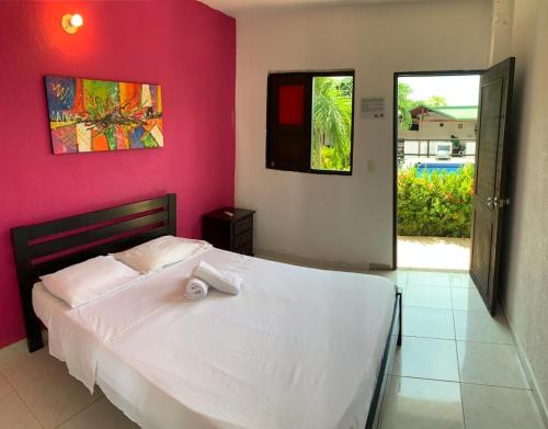 a bedroom with a white bed and a pink wall at La Masia Hostal in Taganga