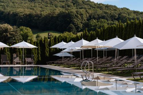 una piscina con sombrillas y sillas blancas en Schlössl Hotel Kindl, en Bad Gleichenberg