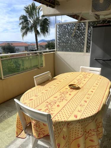 une table et des chaises jaunes sur un balcon avec un palmier dans l'établissement Grand studio vue mer - Plages à pied - Parking, à Antibes
