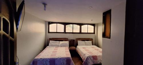 two beds in a small room with two windows at La casa de Mary in Cajamarca