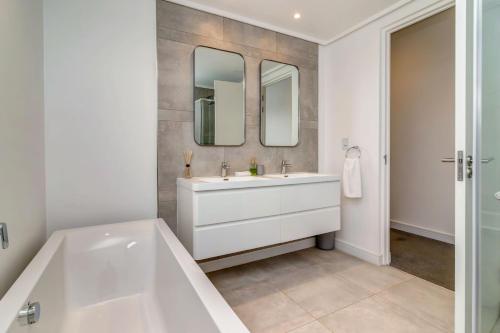 a bathroom with a tub and a sink and two mirrors at Luxurious & Peaceful Sandton 3-bed - Backup Power in Johannesburg