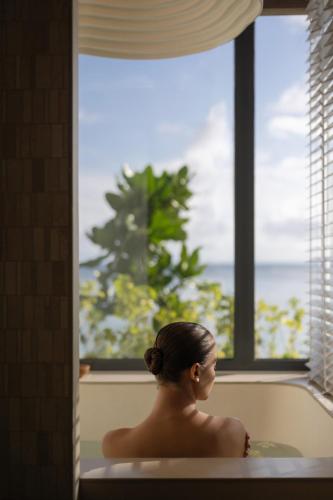 a woman sitting in a bath tub looking out a window at SO/ Maldives in South Male Atoll