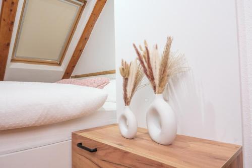 two white vases on a wooden table next to a bed at Apartman Maja in Jajce