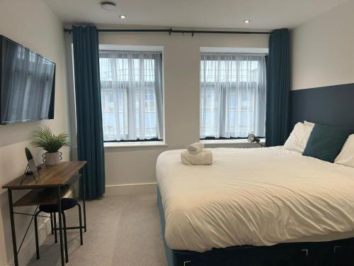 a bedroom with a bed and a desk and windows at Kings Gate House DH ApartHotels in Peterborough