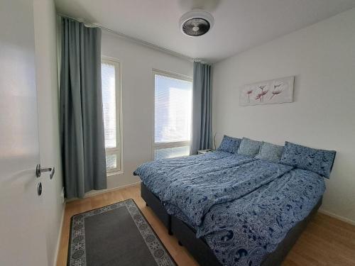 a bedroom with a bed with a blue comforter and two windows at Makasiiniranta in Pori