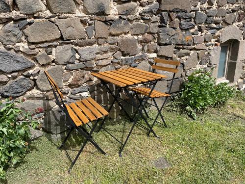 a wooden table and two chairs next to a stone wall at La clé des champs de Laumont in Saint-Diéry
