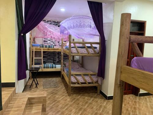 Cette chambre comprend 3 lits superposés avec des rideaux violets. dans l'établissement Mpanga Nature Center, à Mpigi