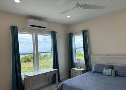 a bedroom with a bed and two large windows at Twin Coves Tranquility: Private Beachfront Estate in North Palmetto Point