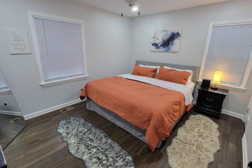 a bedroom with a bed with an orange blanket and two windows at Tranquil Retreat: Short-Term Luxury Rental in Atlanta