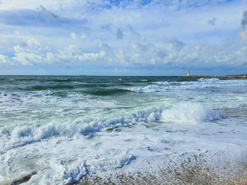 a beach with waves and a lighthouse in the ocean at L'escapade Côte Bleue vue mer panoramique in Sausset-les-Pins