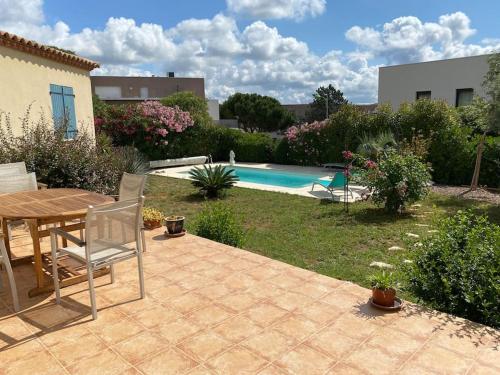 een patio met een tafel en stoelen naast een zwembad bij Jolie villa avec piscine in Juvignac