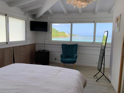 een slaapkamer met een bed, een stoel en ramen bij Villa Clara - Gosier - Vue Mer in Le Gosier