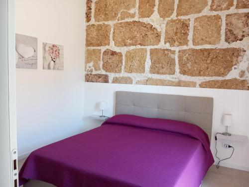 a bedroom with a purple bed with a stone wall at Holiday Home MATT ROS in Noto