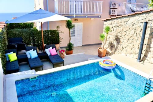 einen Pool mit Stühlen und einem Sonnenschirm neben einem Haus in der Unterkunft Marojica Apartments 2 in Cavtat