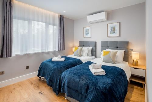 a bedroom with two beds with blue sheets and a window at Two-bedroom flat near Wembley, London in Wealdstone