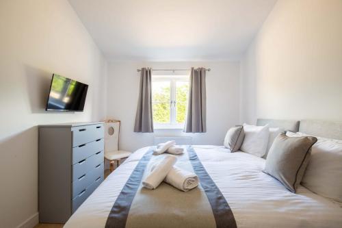 ein Schlafzimmer mit einem weißen Bett, einer Kommode und einem Fenster in der Unterkunft Ascot Cottage in Cirencester