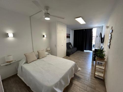 a white bedroom with a bed and a living room at Sunny Apt with terrace coastal area South Arona in Arona