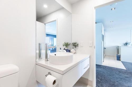 ein weißes Badezimmer mit einem Waschbecken und einem Spiegel in der Unterkunft Serene 2Bed Gem with Free Parking in Auckland