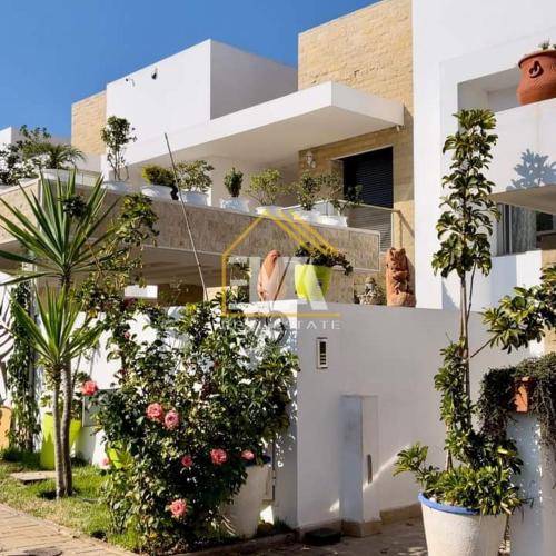 un bâtiment blanc avec des plantes en pot devant lui dans l'établissement Splendide villa prestigia plage des nations, à Sidi Bouqnadel