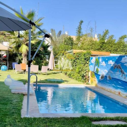 a swimming pool with an umbrella next to a yard at Splendide villa prestigia plage des nations in Sidi Bouqnadel