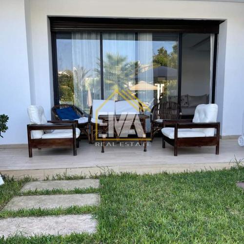 eine Terrasse mit Stühlen, einem Tisch und Fenstern in der Unterkunft Splendide villa prestigia plage des nations in Sidi Bouqnadel