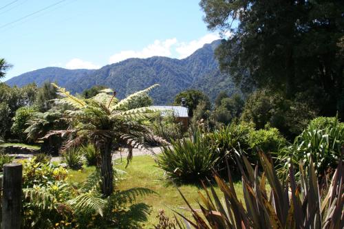 a garden with palm trees and mountains in the background at Westwood Lodge in Franz Josef