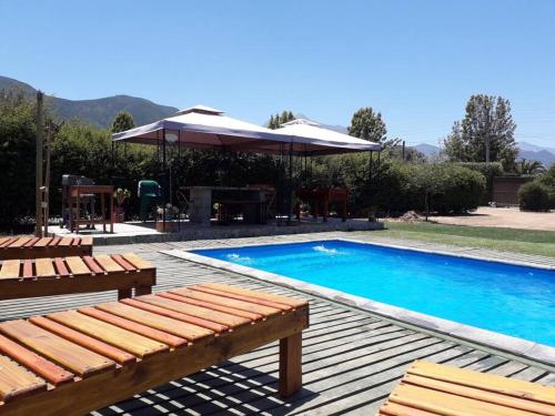 una piscina con 2 bancos y una sombrilla en Acogedora cabaña para disfrutar y descansar, en Olmué