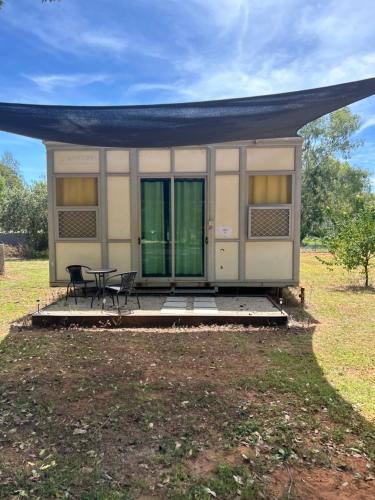 uma pequena casa com uma mesa e cadeiras num campo em Katherine Farmstay Caravan Park em Katherine