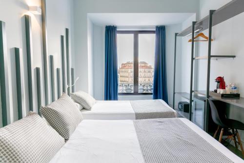 1 dormitorio con 2 camas, escritorio y ventana en Hostal Carmen-Gran Vía, en Madrid